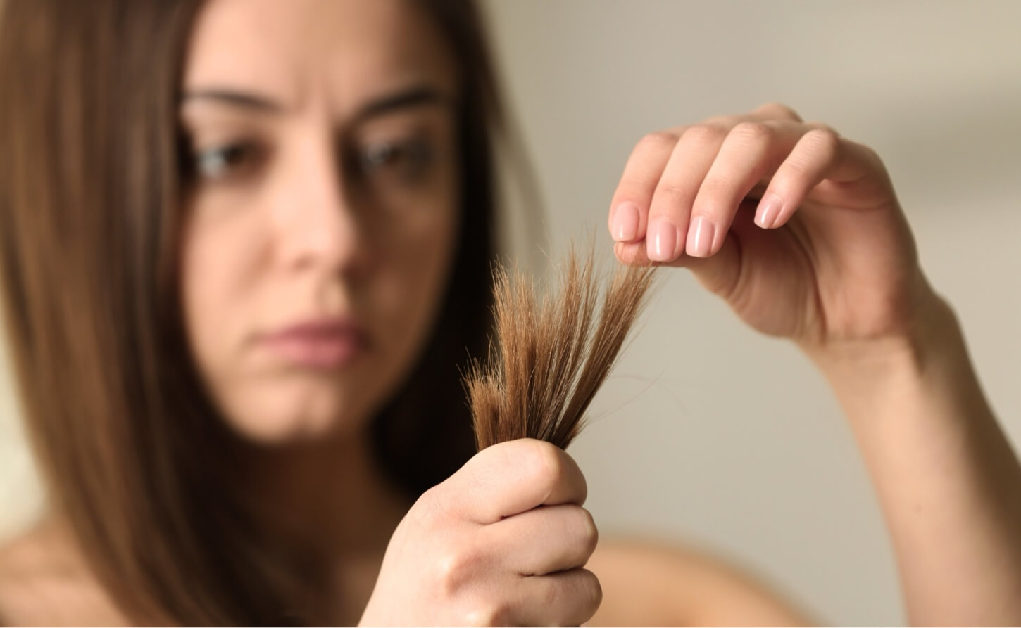 Kvinna tittar bekymrat på kluvna toppar – ett tydligt tecken på att håret saknar näring och behöver vård inifrån.